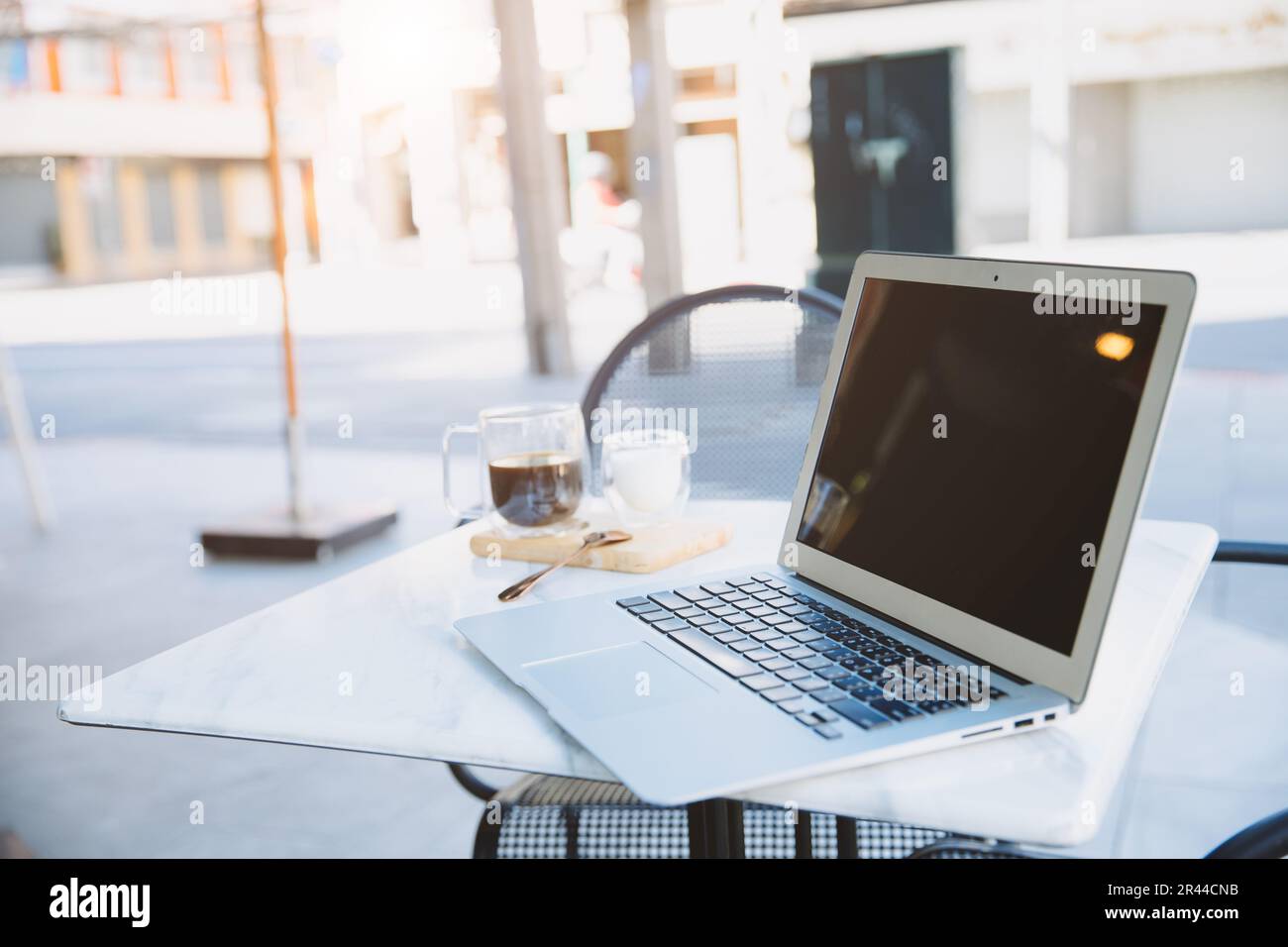 Laptop-Computer am Cafétisch im Freien mit einer Tasse Kaffee für entspanntes Arbeiten, Bürolos, flexibler Arbeitsplatz Stockfoto