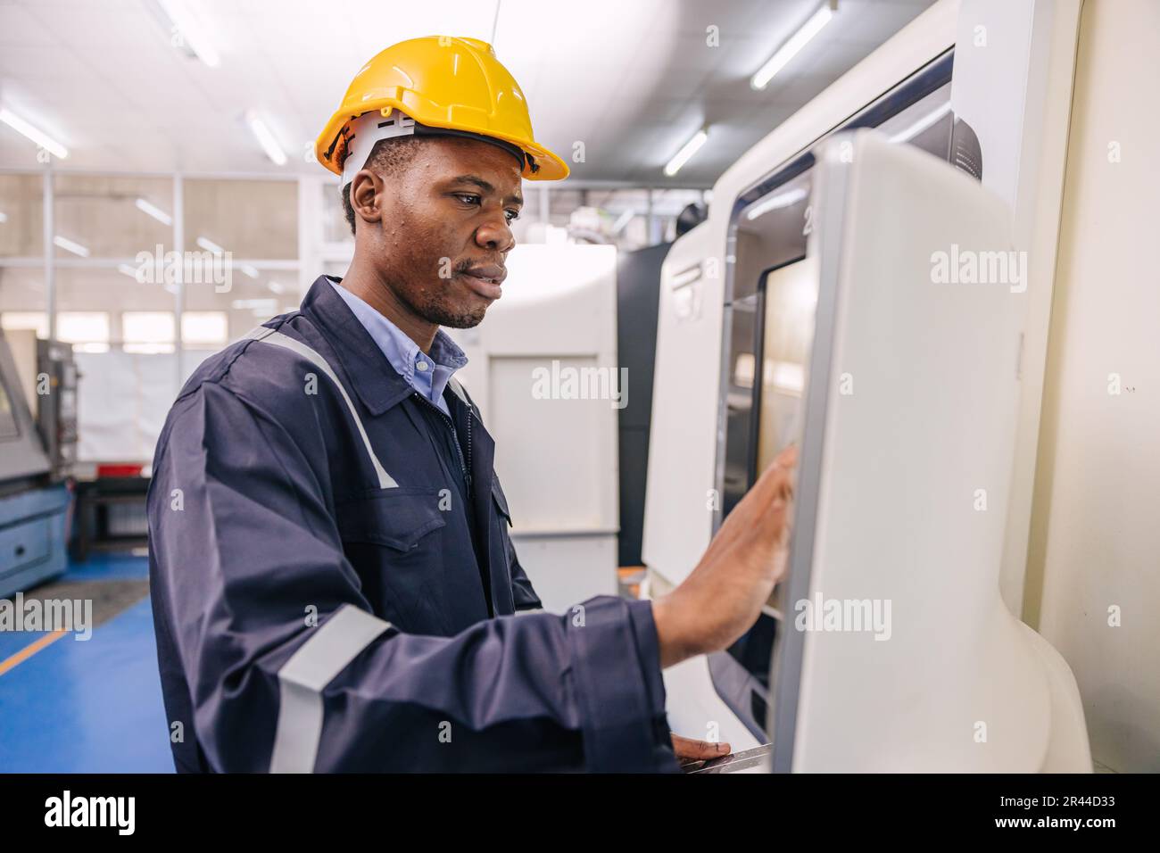 Schwarzer Techniker arbeitet gerne mit der Steuerung moderner CNC-Drehmaschine in der Metallfabrik Stockfoto