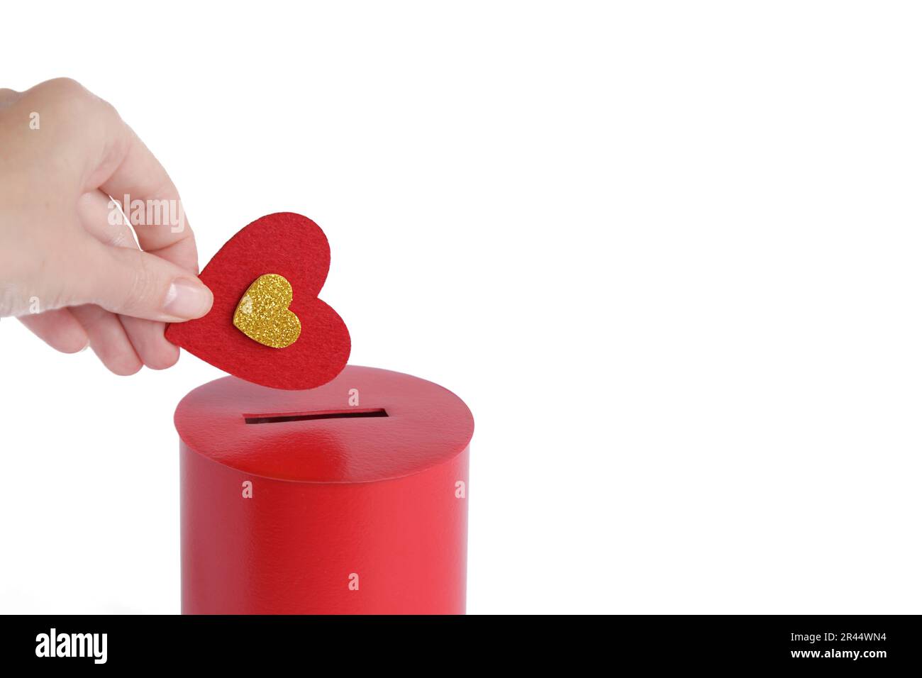 Die Hand steckt Red Heart in die rote Spendenbox. Konzept der aufrichtigen Hingabe zum Glauben. Konzept der Spende, Lebensrettung oder Wohltätigkeit. Nahaufnahme Stockfoto
