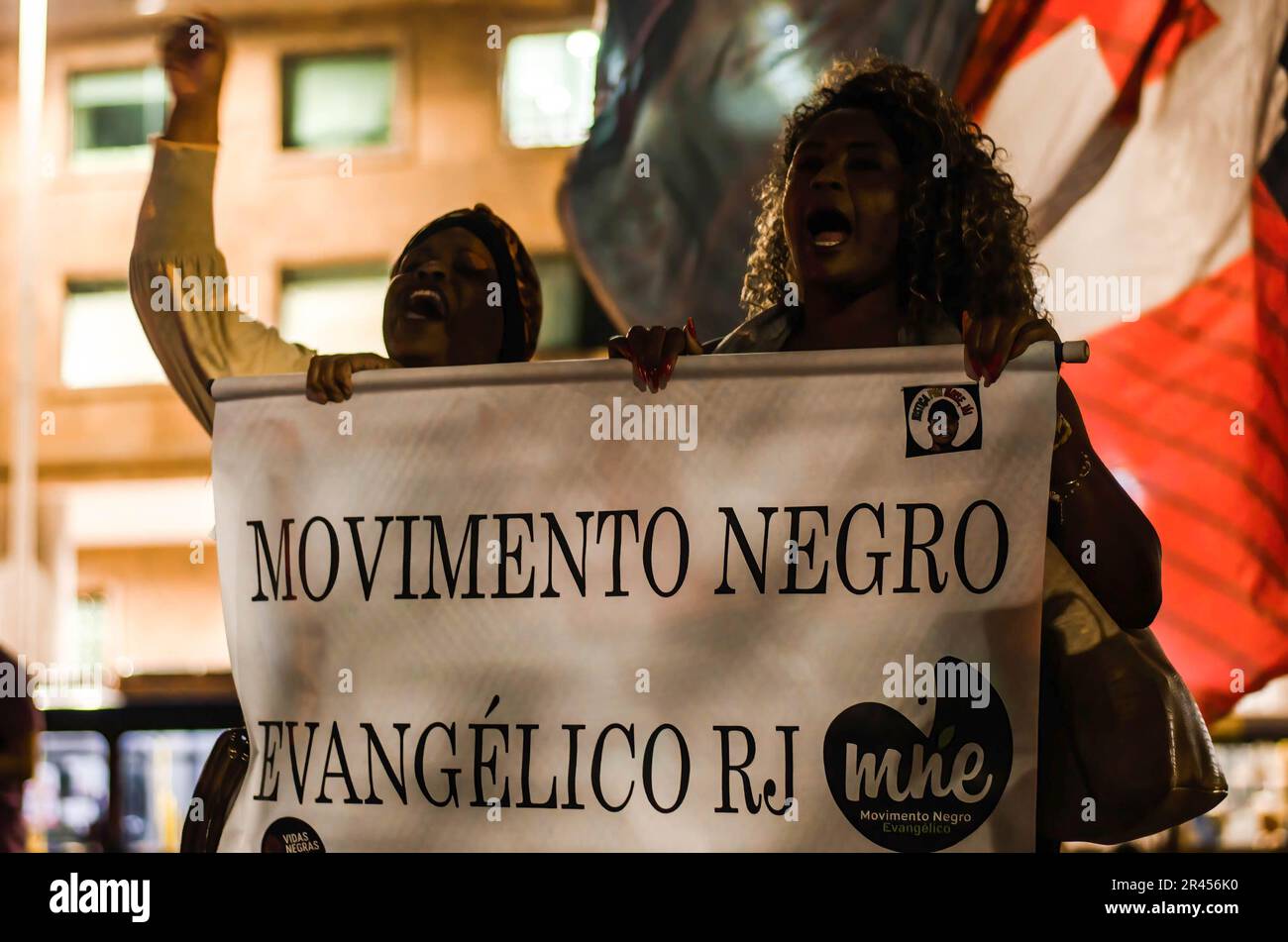 Zwei Frauen halten während der Demonstration ein Banner mit der Aufschrift "religiöse schwarze Bewegung". Manifestation in der Stadt Rio de Janeiro, in Solidarität mit Real Madrids Spieler Vinícius Júnior, der in Spanien während eines Spiels gegen das Team von Valencia am Sonntag (21) Rassismus erlitt. Vinícius Jr. war Opfer von Rassismus und Gewalt, als er während des Spiels von mehreren Fußballfans und Gegnern als „Mono“ (Übersetzung zu „Affe“) bezeichnet wurde. Er wurde später aus dem Spiel geworfen. Vinicius Junior hat bereits acht Fälle von Rassismus, die von La Liga noch bearbeitet werden. Stockfoto
