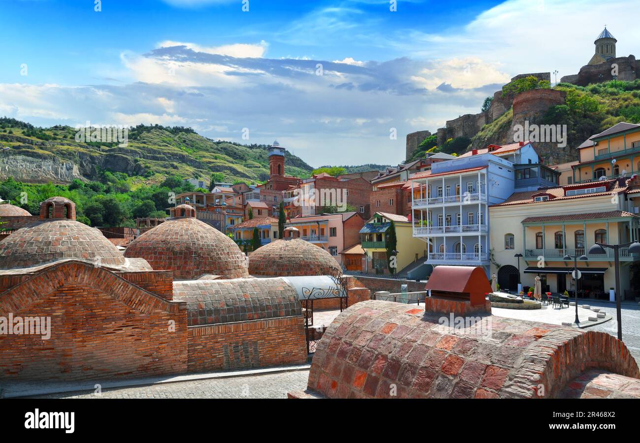 Malerische Aussicht auf antike Schwefelbäder vor blauem Himmel, alte Häuser und die Festung Narikala auf dem Hügel von Tiflis an sonnigen Tagen. Georgien Stockfoto