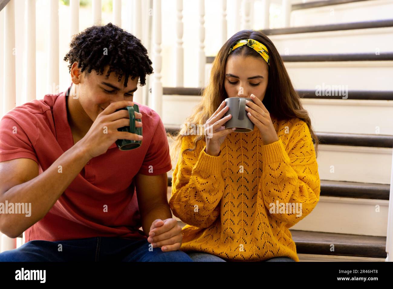 Birassischer junger Freund und Freundin, die Kaffee trinken, während sie zu Hause auf den Stufen sitzen, Kopierraum Stockfoto