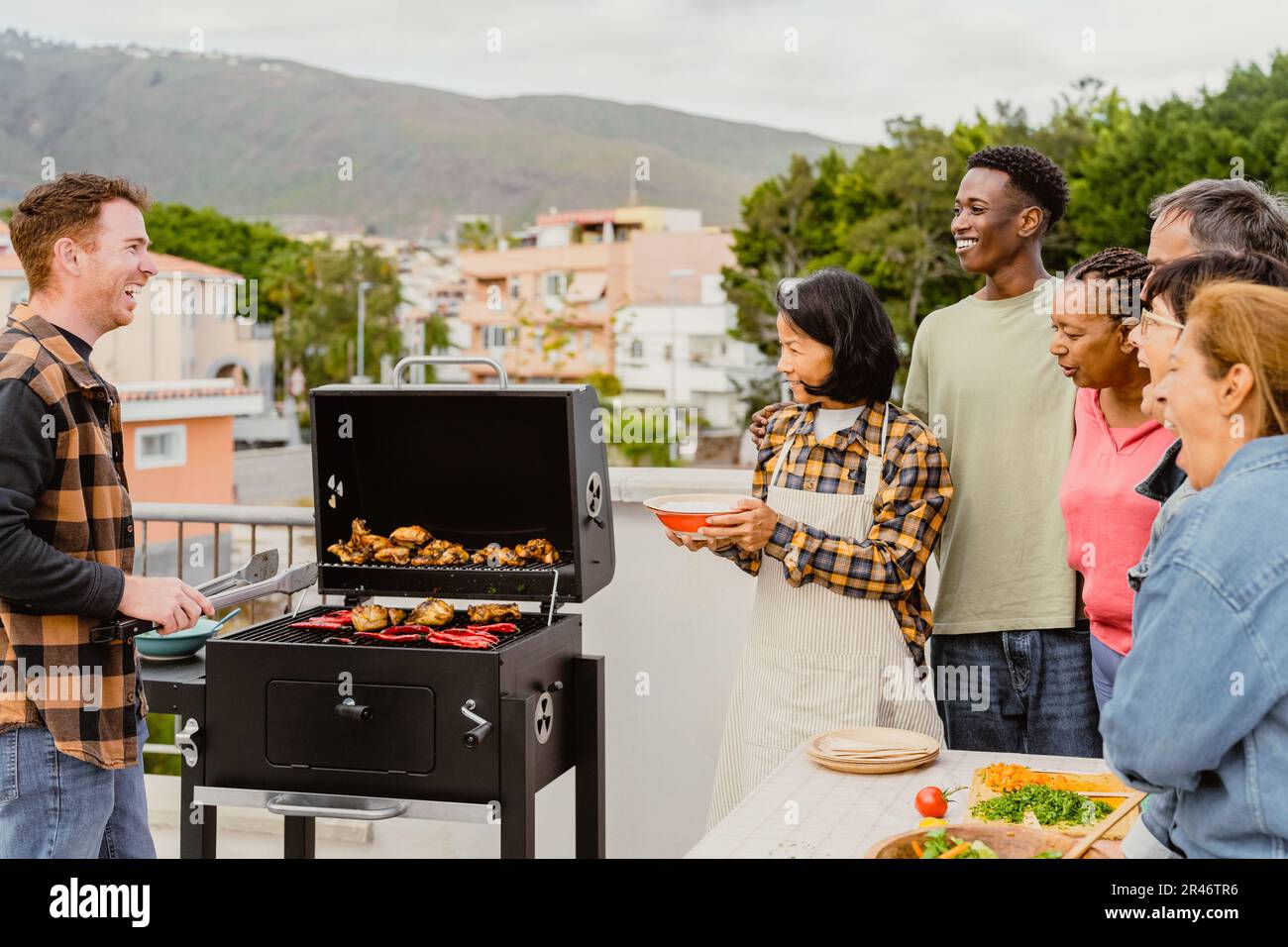 Glückliche, generationenübergreifende Menschen, die Spaß beim Grillen auf dem Dach des Hauses haben - Sommerversammlungen und Essenskonzept Stockfoto