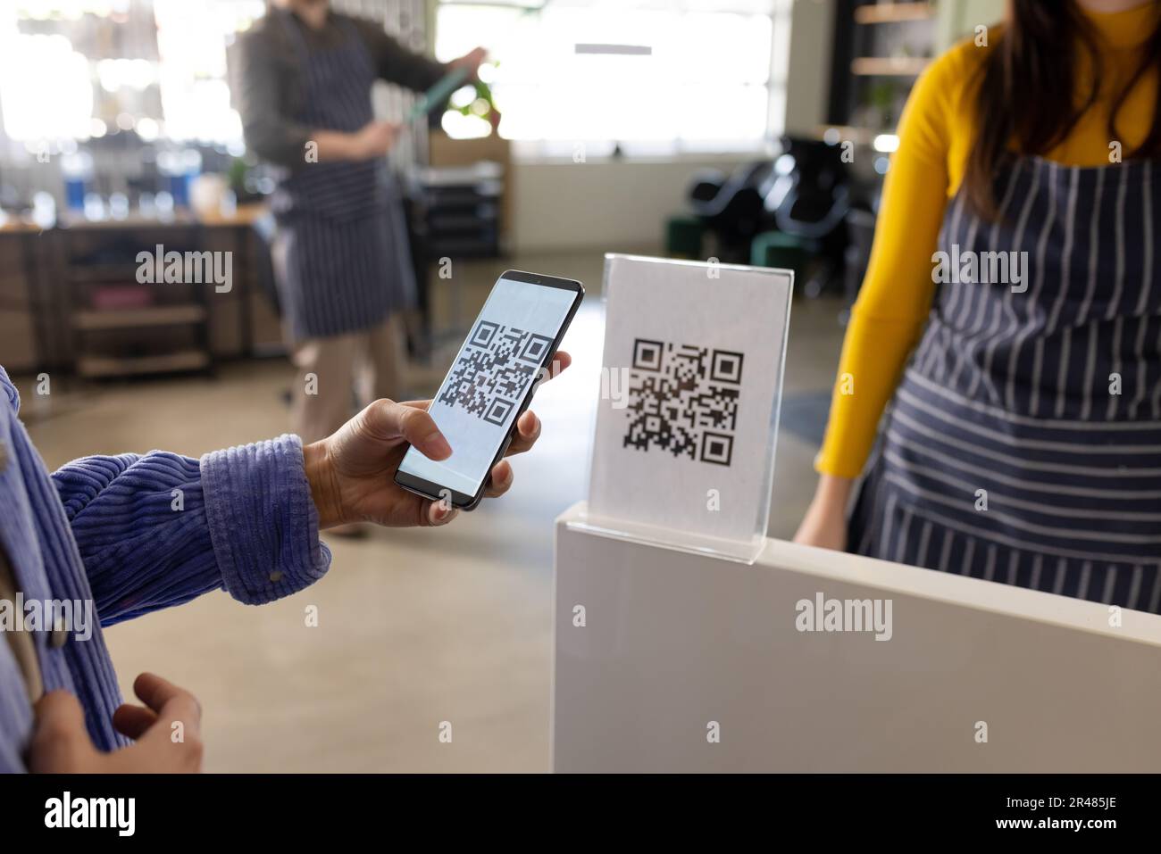 Mittelschnitt einer weissen Klientin, die qr-Code mit Smartphone im Friseursalon scannt Stockfoto