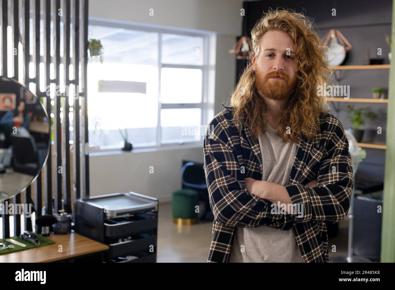 Porträt eines glücklichen weißlichen männlichen Kunden mit langen lockigen roten Haaren und Bart im Friseursalon Stockfoto