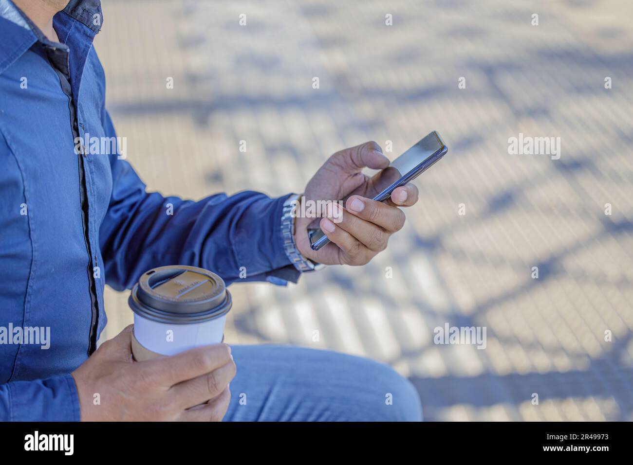 Detail der Hände eines Mannes mit einem Handy und einer Papptasse Kaffee. Stockfoto
