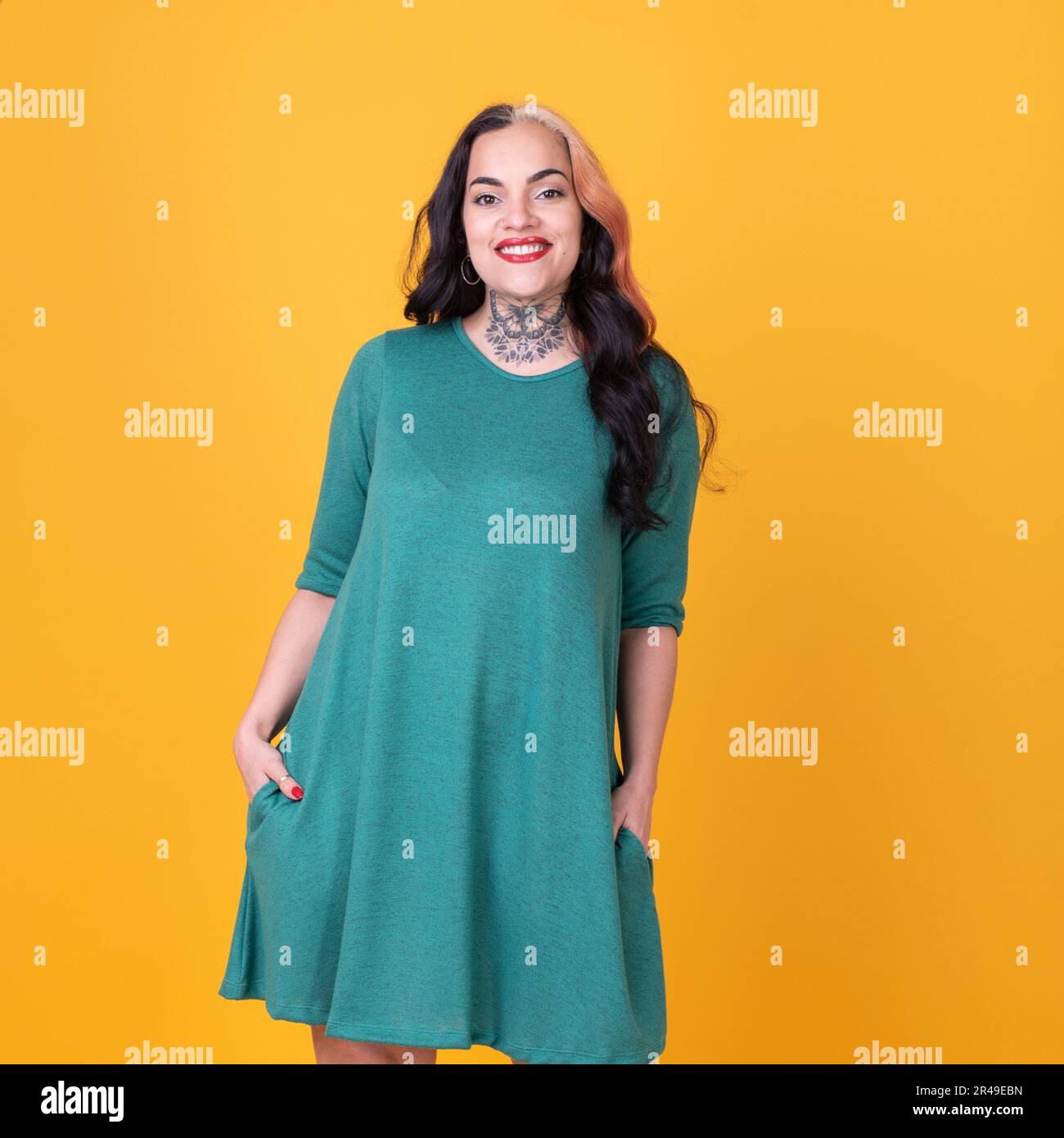 Schöne Frau in einem grünen Kleid, die auf einen gelben Hintergrund in die Kamera schaut. Studioaufnahme Stockfoto