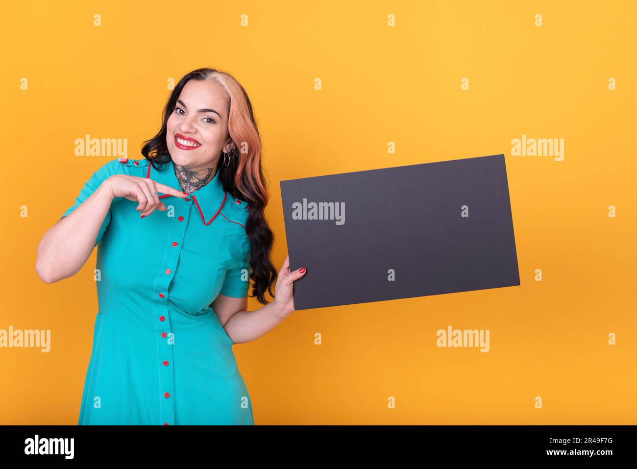 Schöne Frau, die auf ein leeres schwarzes Brett vor gelbem Hintergrund zeigt Stockfoto