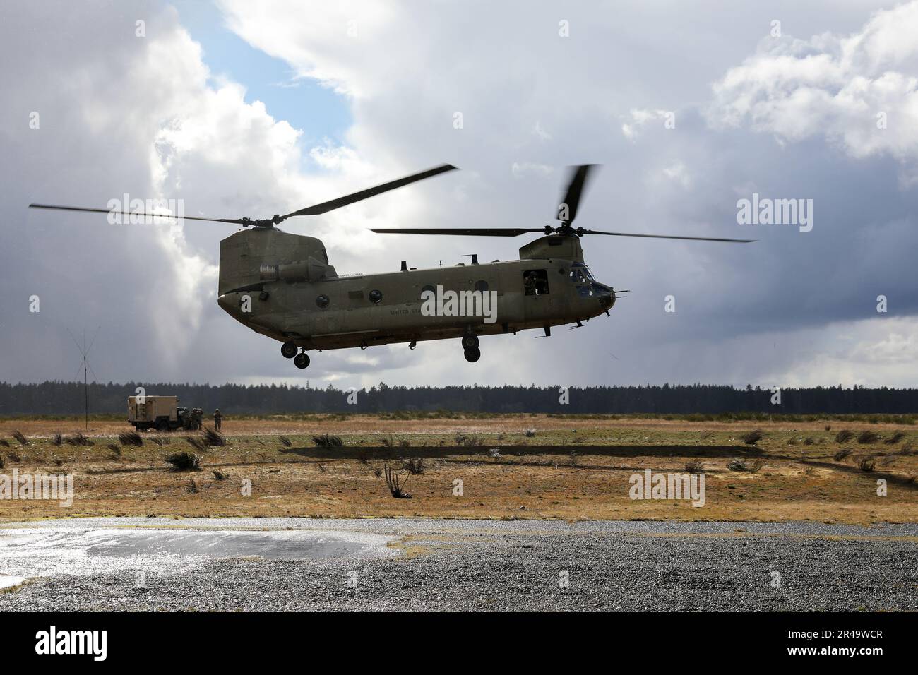 Ein Ch-47 Chinook Helicopter schweben über dem Boden, um die Last eines M777 155-mm-Haubitzers an eine zweite Zündposition auf der Joint Base Lewis McChord, Washington, zu transportieren. 1. April 2023. Stockfoto