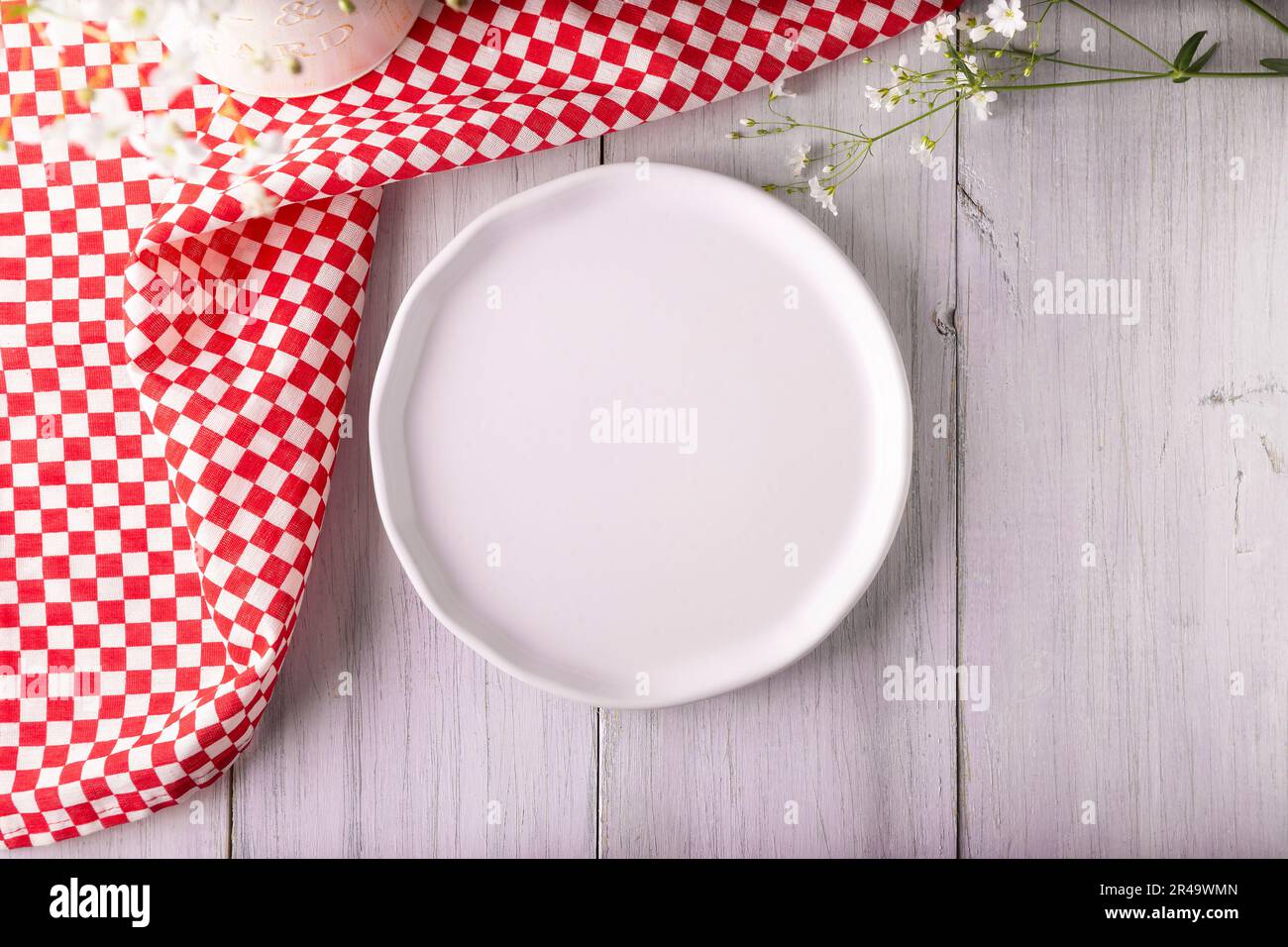Kochhintergrund mit leerem weißem Teller und Picknick-Tischdecke auf rustikalem weißen Holztisch. Tabellenansicht mit Kopierbereich. Stockfoto