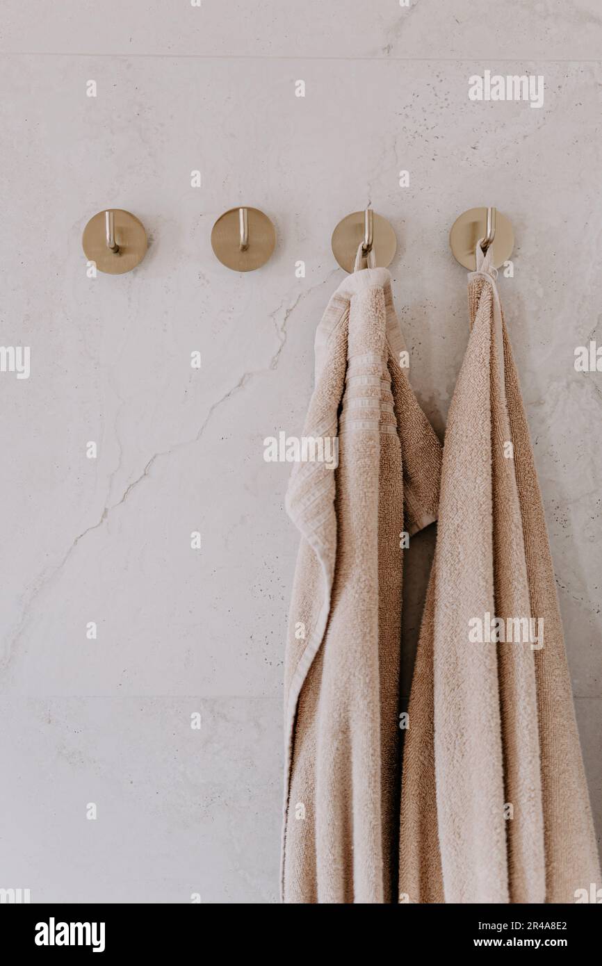 Eine stilvolle weiße Marmorwand mit zwei weichen Handtüchern und vier Metallhaken, perfekt für jede Inneneinrichtung Stockfoto
