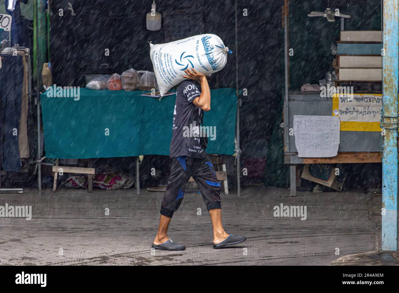 SAMUT PRAKAN, THAILAND, MAI 10 2023, Ein Mann trägt eine Tasche Eis auf einem Markt bei starkem Regen Stockfoto