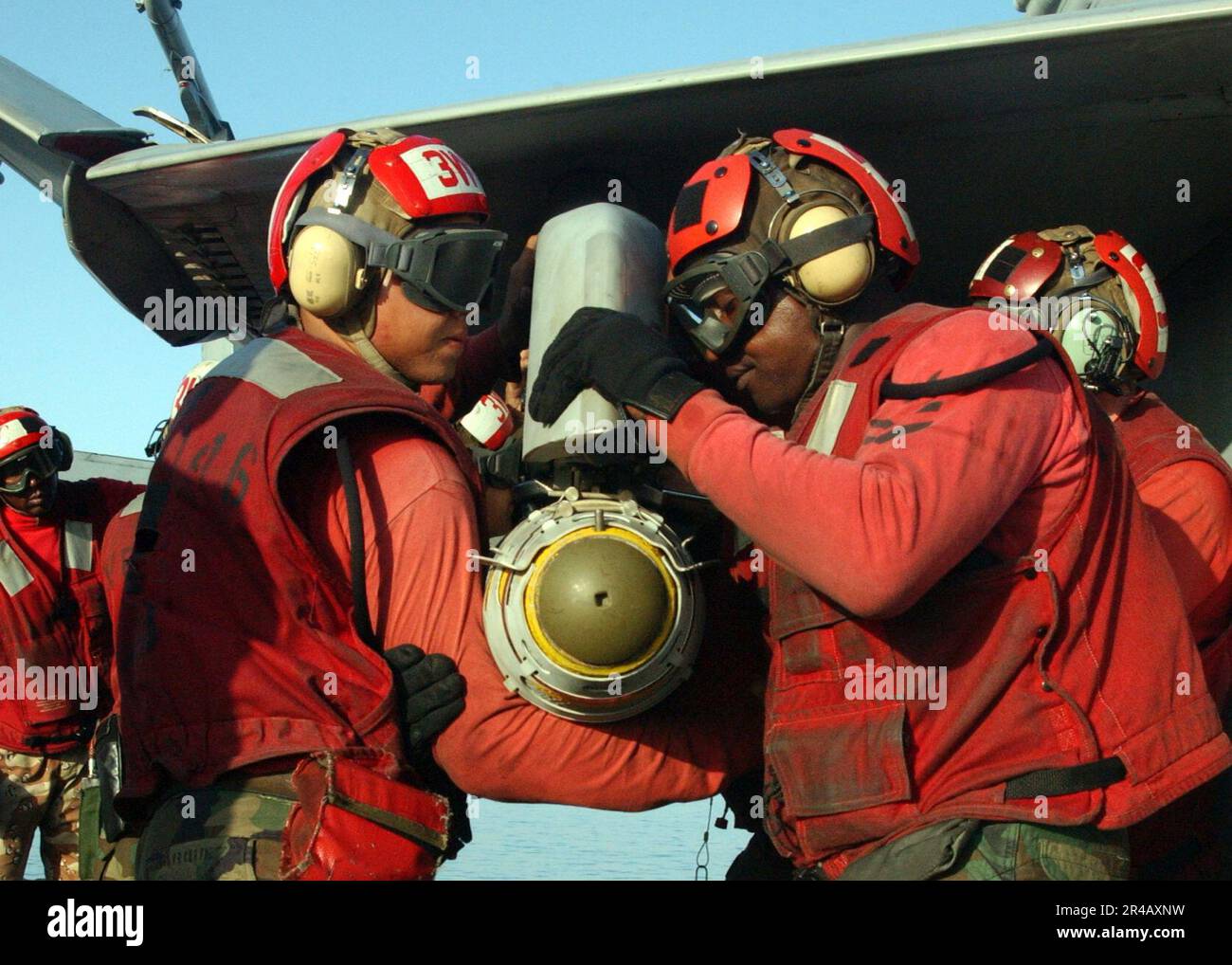 US Navy Aviation Ordnancemen entladen eine GBU-38 500 Pfund Satelliten-gesteuerte Bombe aus dem Flügel einer F-A-18C Hornet. Stockfoto