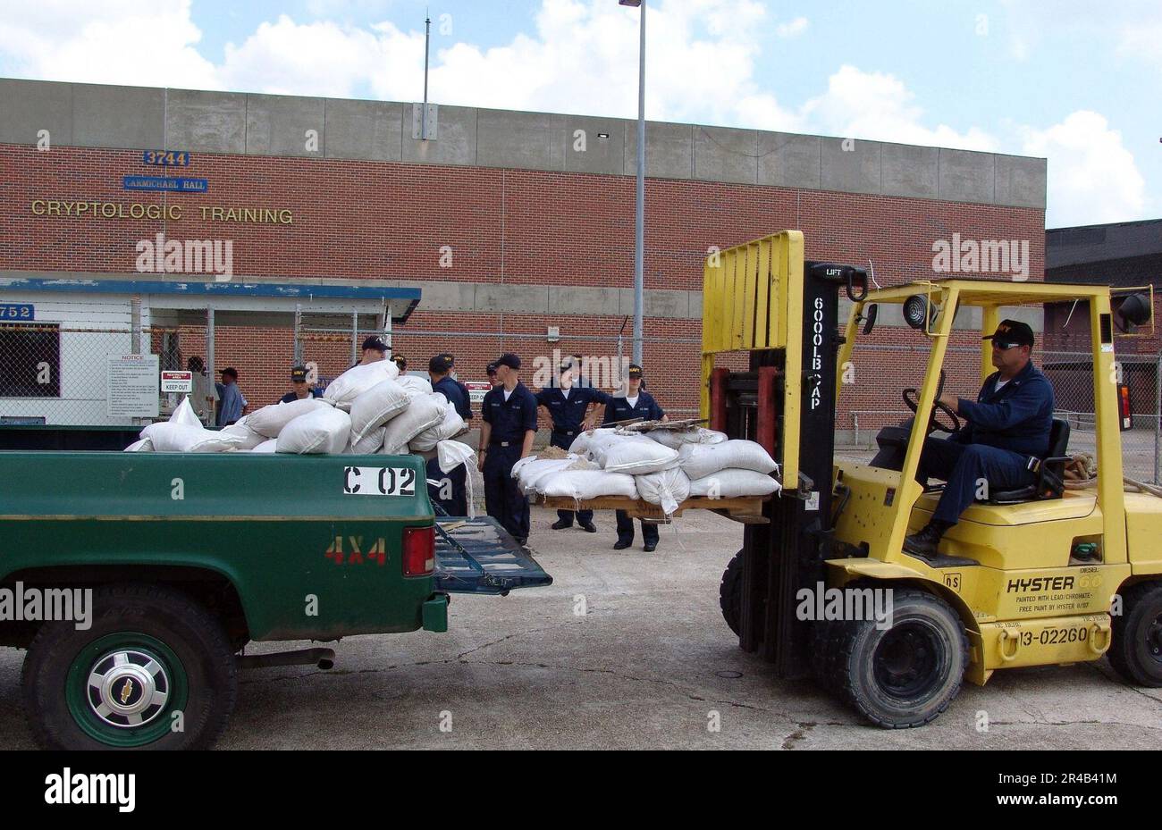 US Navy Cryptological Technician 1. Class entlädt Paletten mit Sandsäcken am Center for Information Dominance, Corry Station, während sich die wartenden Seeleute darauf vorbereiten, sie um die Außentüren herum zu platzieren Stockfoto