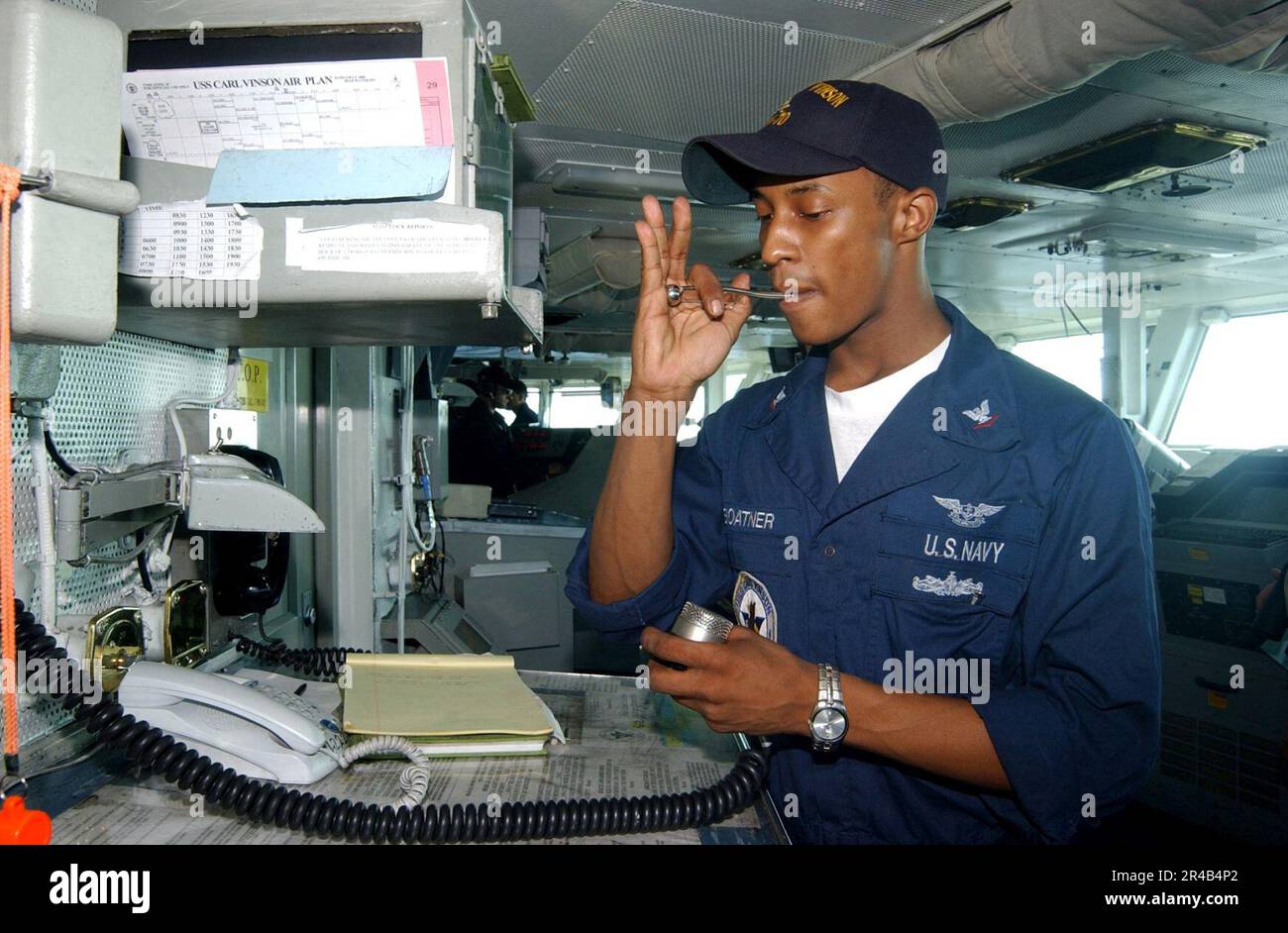 US Navy Boatswain's Mate 3. Class pfeift über die 1MC und signalisiert den Beginn der morgendlichen Ankündigungen, während Boatswain Mate von der Uhr steht. Stockfoto