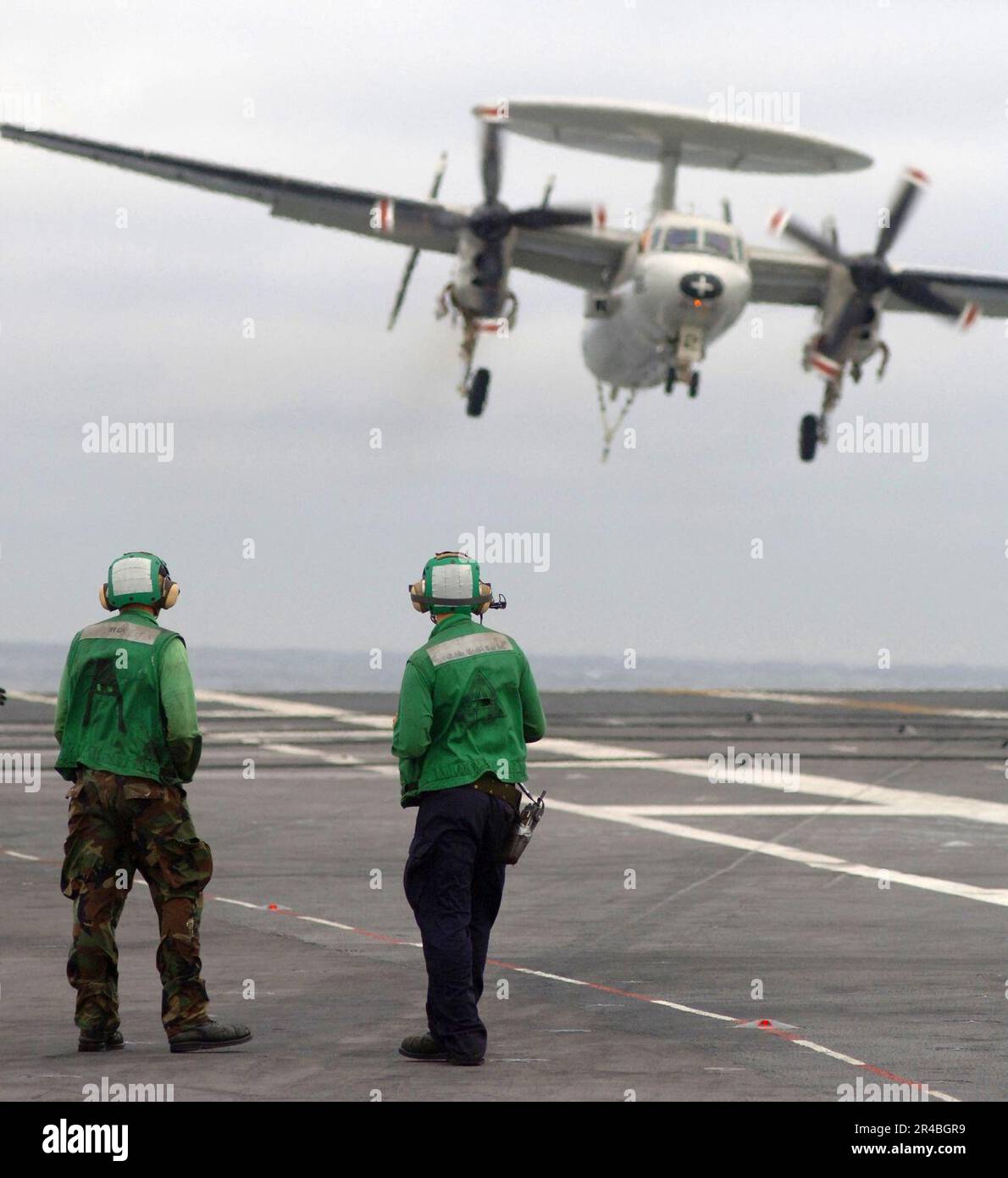 Personal des US Navy Air Department beobachtet, wie ein E-2C Hawkeye, der den Seahawks des Flugzeugträger-Frühwarngeschwaders One Two Six (VAW-126) zugeteilt wurde, sich nähert, um eine festgenommene Genesung durchzuführen. Stockfoto