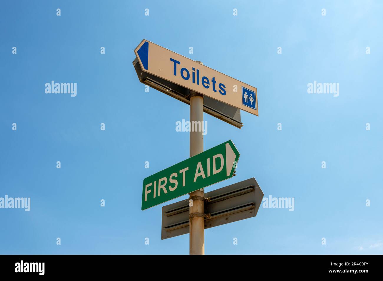 Erste-Hilfe- und Toilettenschilder auf einem Metallschild vor einem blauen Himmel Stockfoto