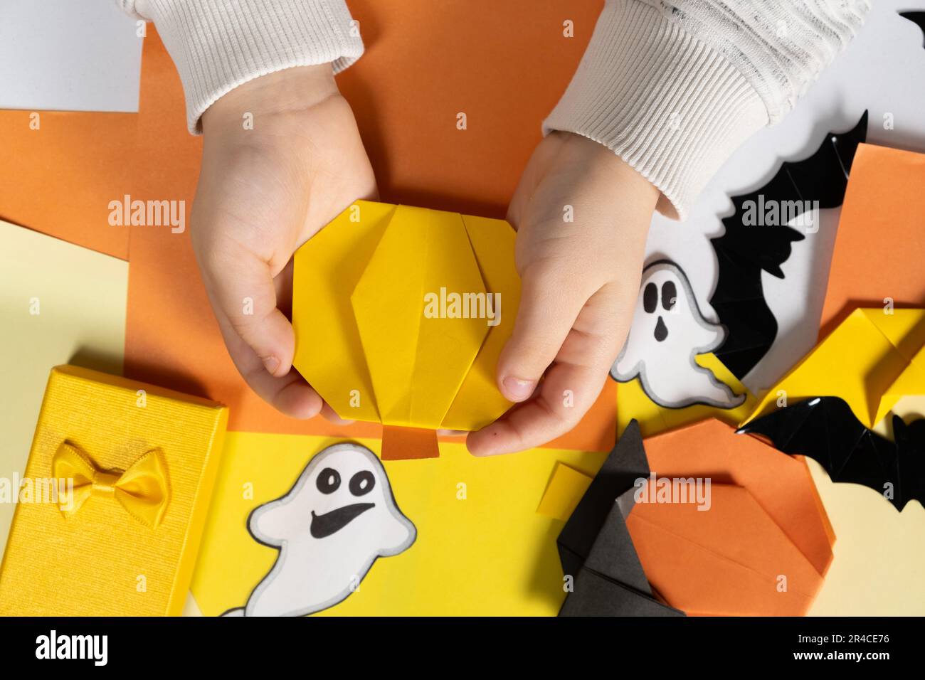 Origami Basteln für Halloween - Kürbis aus Papier in den Händen eines Kindes, Draufsicht. Stockfoto