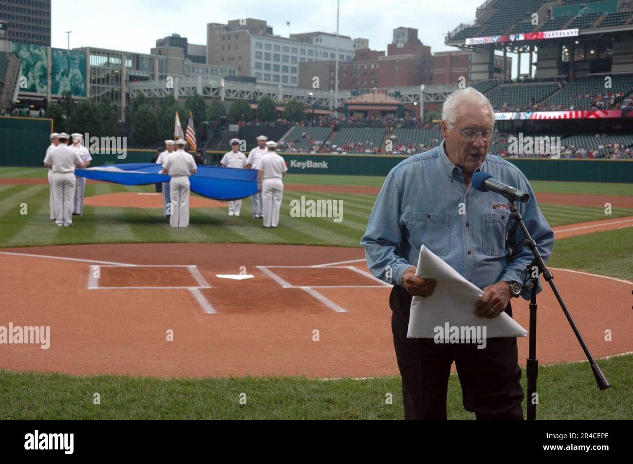 US Navy Major League Baseball Hall of Fame Inductee und Veteran der Marine aus dem Zweiten Weltkrieg akzeptieren eine Cleveland Indians Chief Wahoo Logo Flagge, die ihm vom Amphibienschiff USS Cleveland überreicht wird. Stockfoto