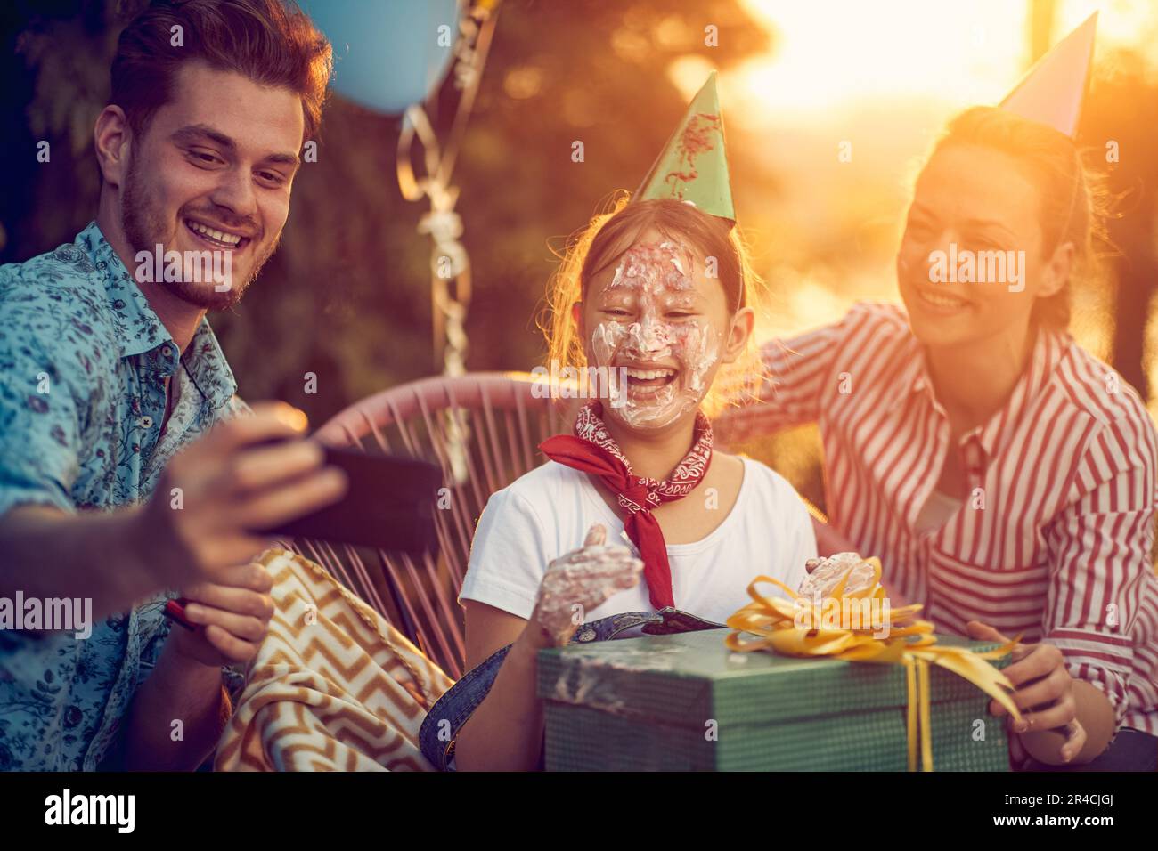 Liebevolle Familie, mit Tochter, Mutter und Vater, die zusammen Geburtstag feiern. Der Vater, der ein Smartphone in der Hand hält, wird dabei gesehen, wie er geschickt ein Selfie macht Stockfoto