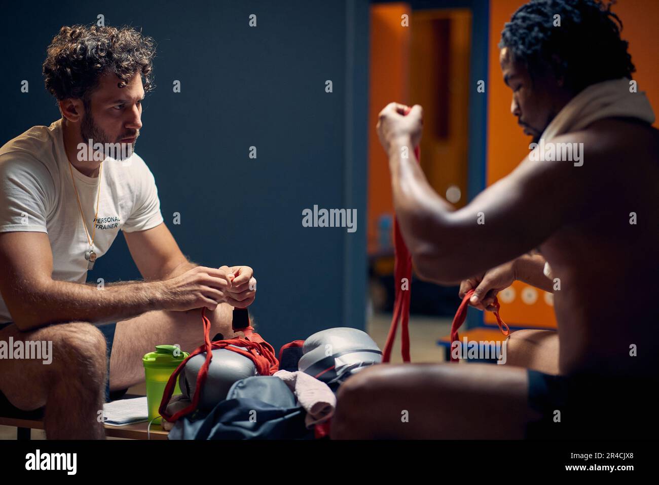 Junger Boxspieler, der mit seinem Trainer in der Garderobe sitzt und sich auf das Boxtraining vorbereitet. Sport-, Wellness-, Lifestyle-Konzept. Stockfoto