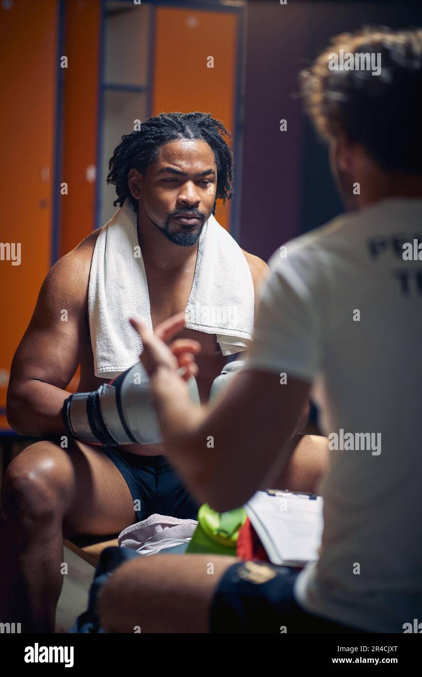 Junger Boxspieler sitzt in der Garderobe von Angesicht zu Angesicht und der Trainer spricht. Beratung nach dem Training. Stockfoto