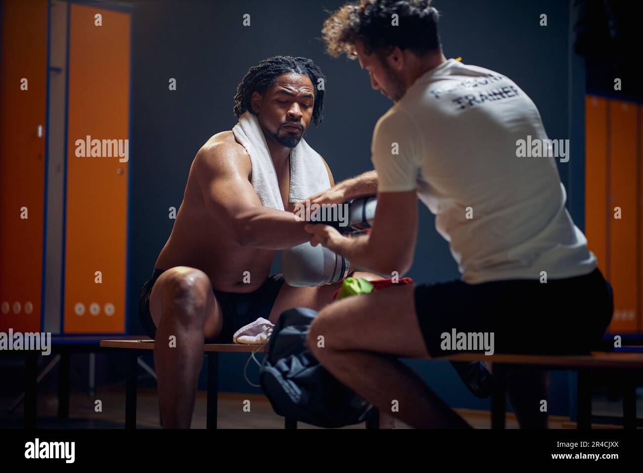 Ein persönlicher Trainer hilft dem Boxspieler, seine Boxhandschuhe nach dem Training auszuziehen und sich in der Garderobe auszuruhen. Sport, Lifestyle-Konzept. Stockfoto