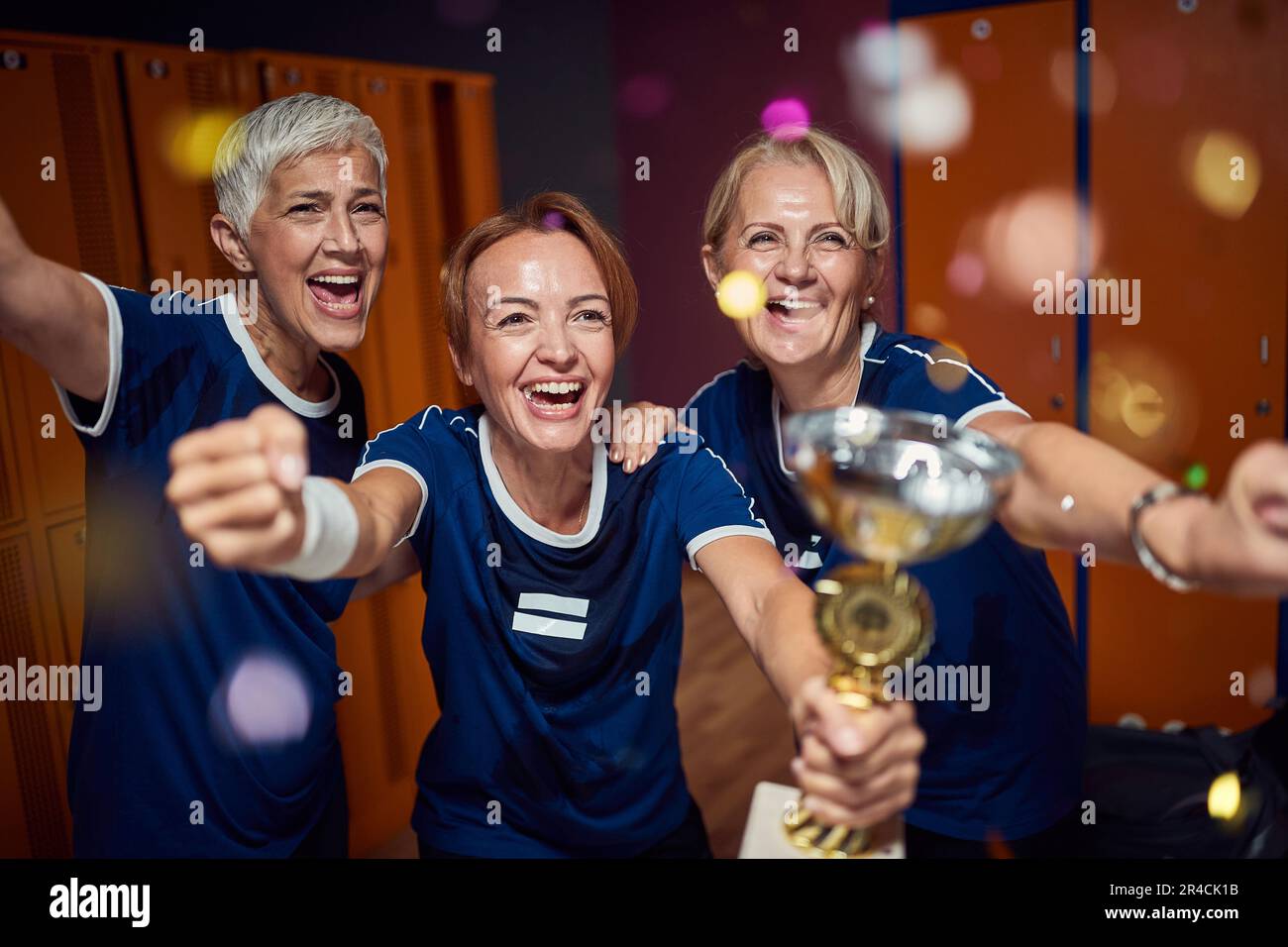 Team aus erwachsenen Frauen und jungen Trainern in Sportkleidung, die den goldenen Becher gewonnen haben, sich siegreich fühlen. Stockfoto