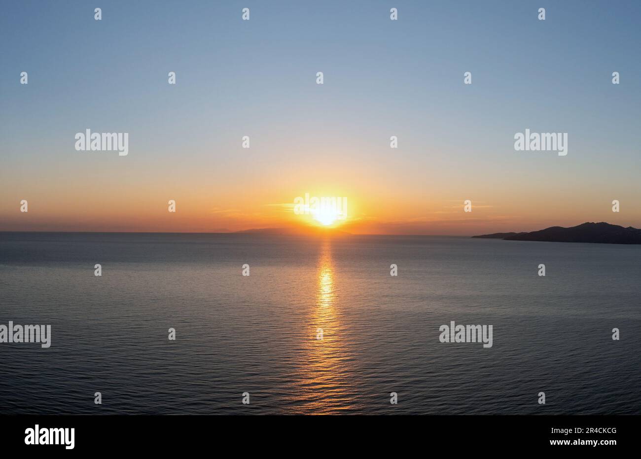 Sonnenuntergang über der griechischen Insel, Kykladen, Griechenland. Die Goldene Sonne versteckt sich hinter dem Hügel bei Sonnenuntergang und die Farben vergolden das ruhige, weite blaue Meerwasser der Ägäis. Stockfoto