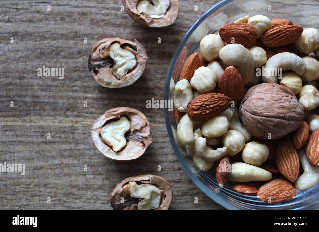 Nüsse Mischung aus Mandeln, Haselnüssen und Cashews in einer Glasuntertasse und Walnüsse in zwei Hälften geteilt Stockfoto