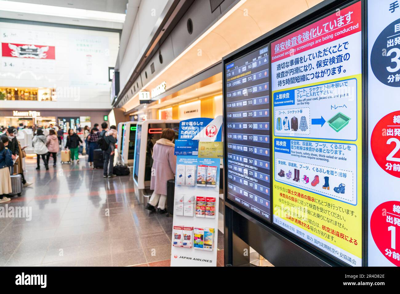 Videoanzeige an der Wand über verbesserte Sicherheitskontrollen und Informationen zum Abflug, Hintergrund, unscharfe Personen, die Gepäck aufgeben. Haneda Air Stockfoto