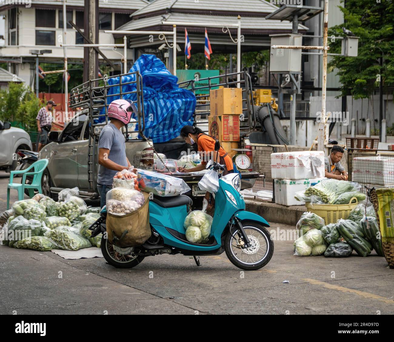 Ein Großhändler für Gemüsegüter stellt eine Rechnung für einen Kunden aus, der mit seinem Motorrad auf der angrenzenden Straße des Bangkok Flower Market (Pak Khlong Talat) am Fluss Chao Phraya auf der Insel Rattanakosin im Bezirk Phra Nakhon wartet. Bangkok Flower Market (Pak Khlong Talad) Thailands größter Blumengroßmarkt, 24 Stunden am Tag, 7 Tage die Woche geöffnet, neben einem Markt für frisches Gemüse, Obst und Kräuter, an der Chak Phet Road, in der Nähe der Gedächtnisbrücke (Saphan Phut) in der historischen Altstadt. Stockfoto