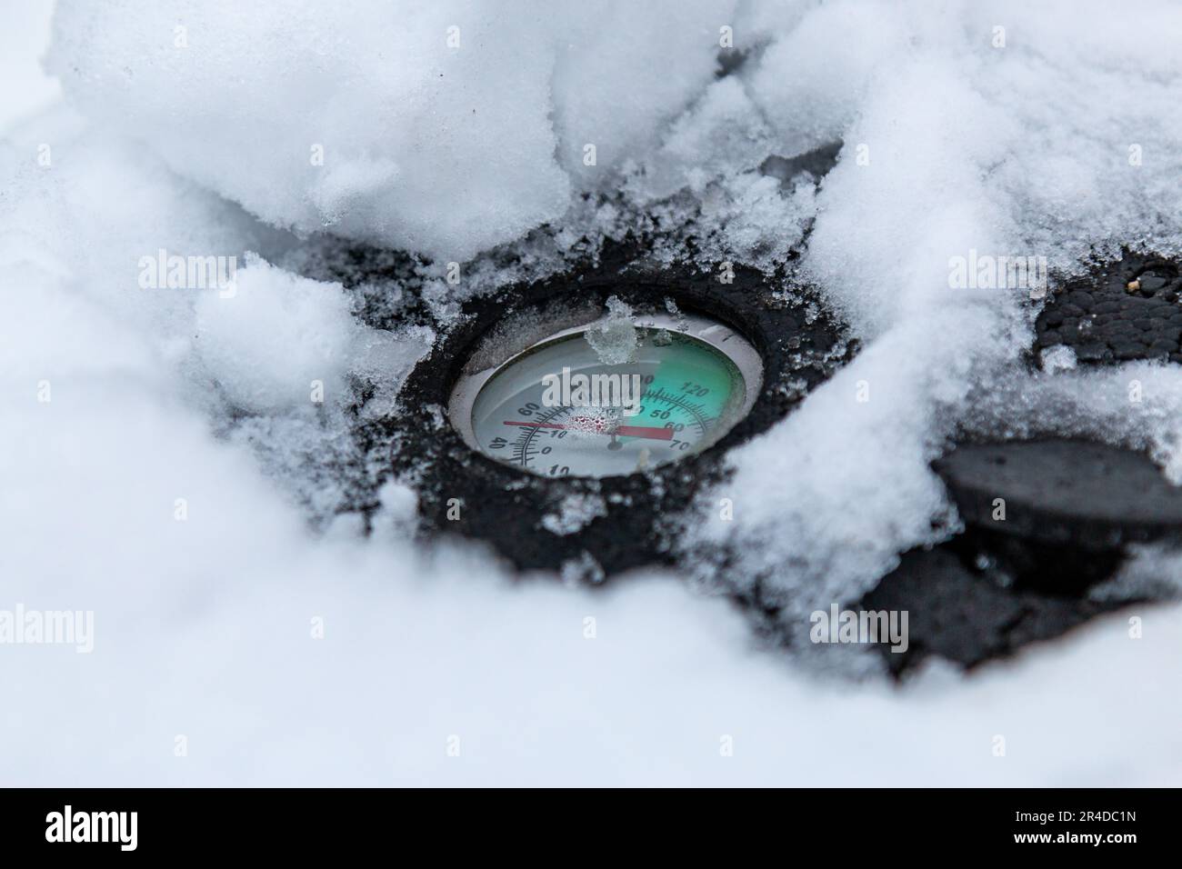 Das Thermometer auf dem Deckel eines im Winter mit Schnee bedeckten Kompost-Behälters zeigt, dass der Inhalt des Behälters kalt ist, Cambridge, Großbritannien. Stockfoto