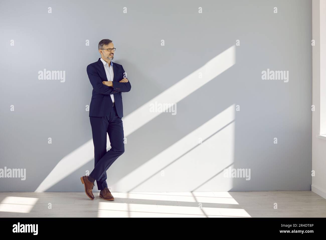 Ein gutaussehender Geschäftsmann mittleren Alters, der sich gegen die graue Wand lehnt Stockfoto