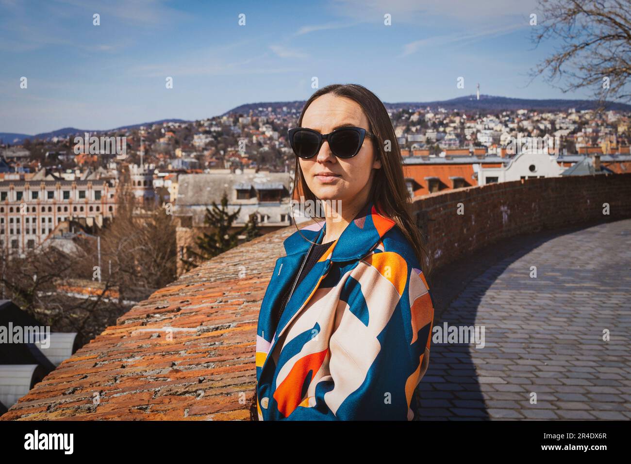 Junge Frau mit Sonnenbrille in einer farbenfrohen Jacke mit Budapest im Hintergrund Stockfoto