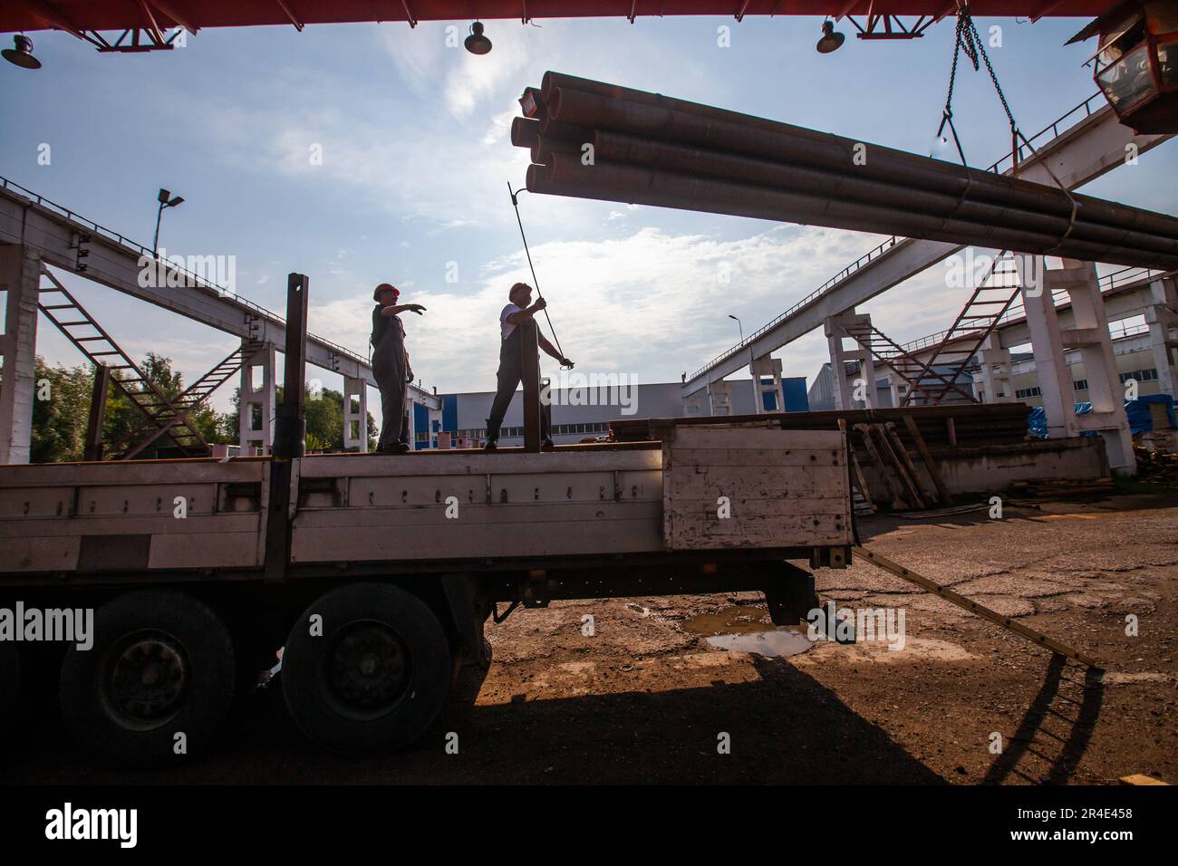 Podolsk, Provinz Moskau - 02. August 2021: Rohrlager. Silhouetten von Arbeitern, die Rohre mit Brückenkranen verladen Stockfoto