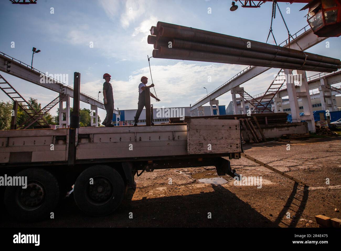 Podolsk, Provinz Moskau - 02. August 2021: Silhouetten von Arbeitern, die Rohre mit einem Brückenkran beladen. Rohrlager. Stockfoto