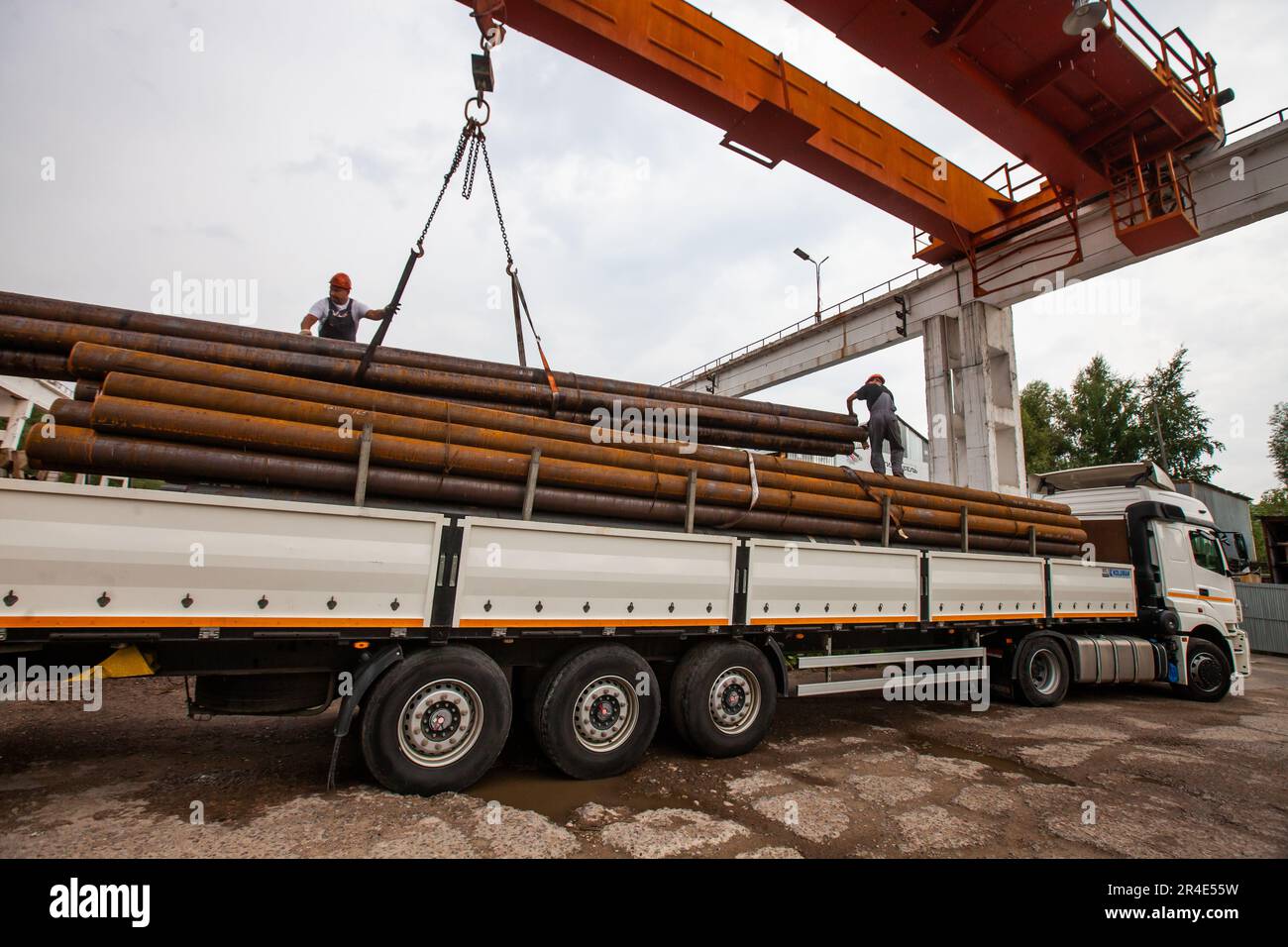 Podolsk, Provinz Moskau - 02. August 2021: Rohrlager. Zwei Arbeiter verladen Rohre in einen Lkw mit Brückenkran Stockfoto