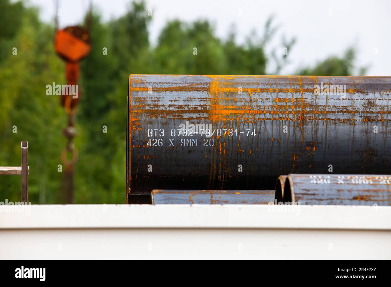 Stahlrohr mit etwas Rost auf Außenlagerung. Bäume und Kranhaken im Hintergrund, verschwommen Stockfoto