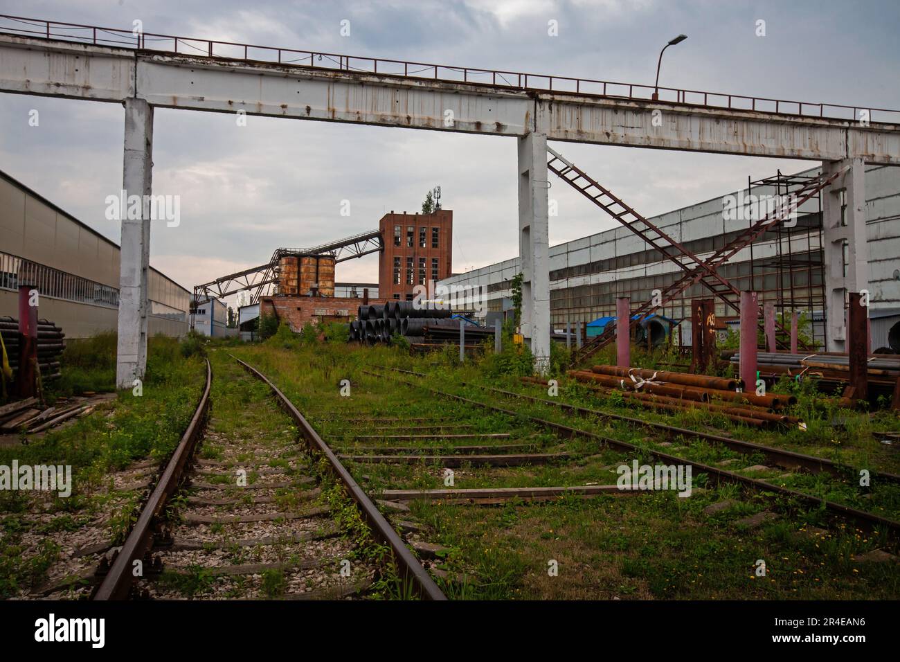 Veraltete sowjetische Fabrik. Schienen, Betonkranbrücke und Ziegelturm mit zerbrochenen Fenstern Stockfoto
