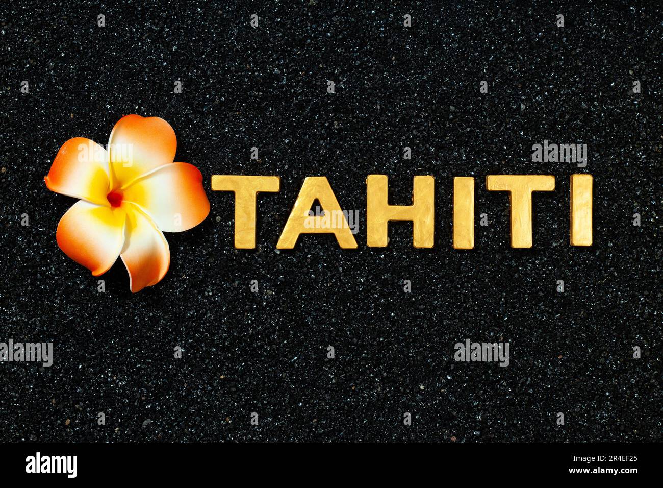 Tahiti: Goldene Buchstaben in schwarzem Sand und Plumeria-Blume Stockfoto