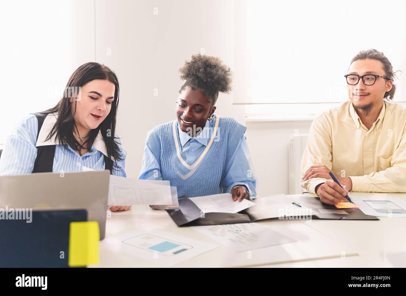 Ein vielseitiges Team von Kollegen, darunter eine Chinesin, eine Afroamerikanerin und eine Kaukasierin, die Ideen an einem Schreibtisch diskutieren. Die weiße Frau hat Papiere Stockfoto
