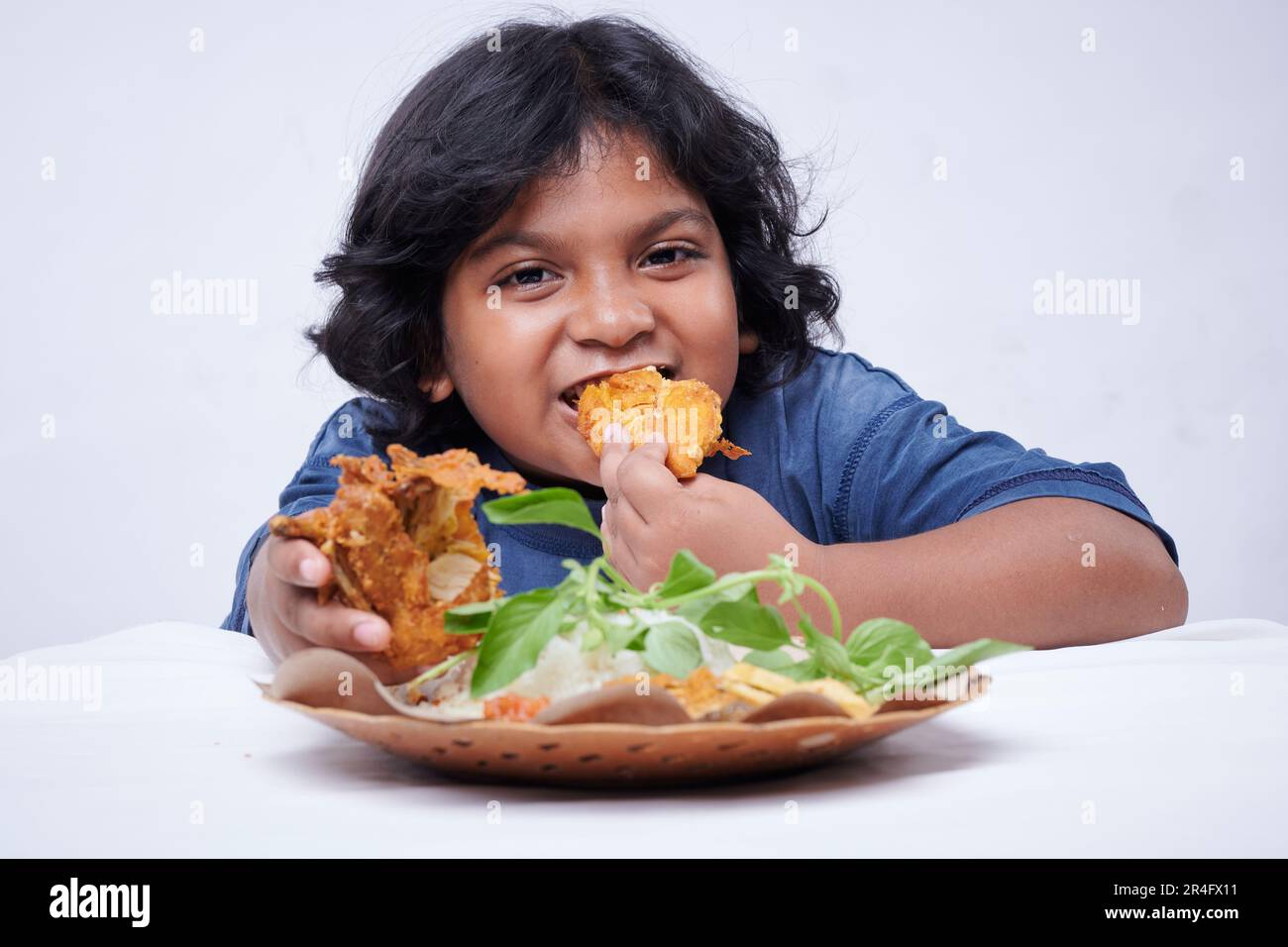 Ein kleines Mädchen, das gebratenes Hühnchen isst, Reis mit Gemüse und scharfem Souce Stockfoto