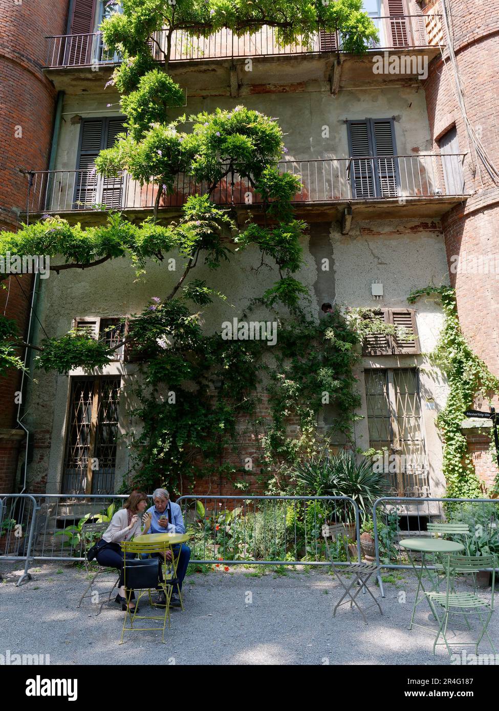 Das Paar sitzt im Botanischen Garten von Brera mit Gebäude und Baum dahinter, Stadtteil von Brera, Mailand, Lombardei, Italien Stockfoto
