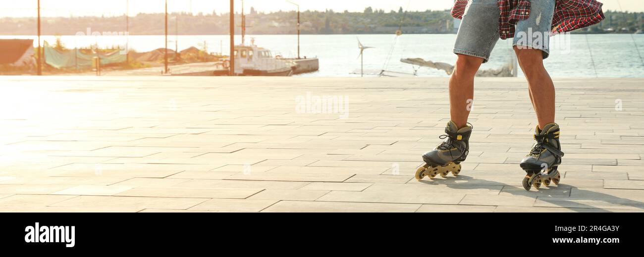 Junger Mann, der Rollschuhlaufen auf dem Pier in der Nähe des Flusses macht, Platz für Text. Bannerdesign Stockfoto