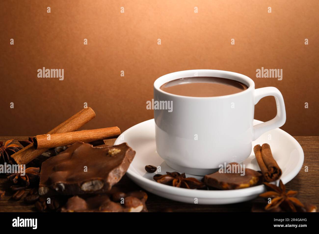 Eine Tasse köstliche heiße Schokolade, Gewürze und Kaffeebohnen auf einem Holztisch Stockfoto