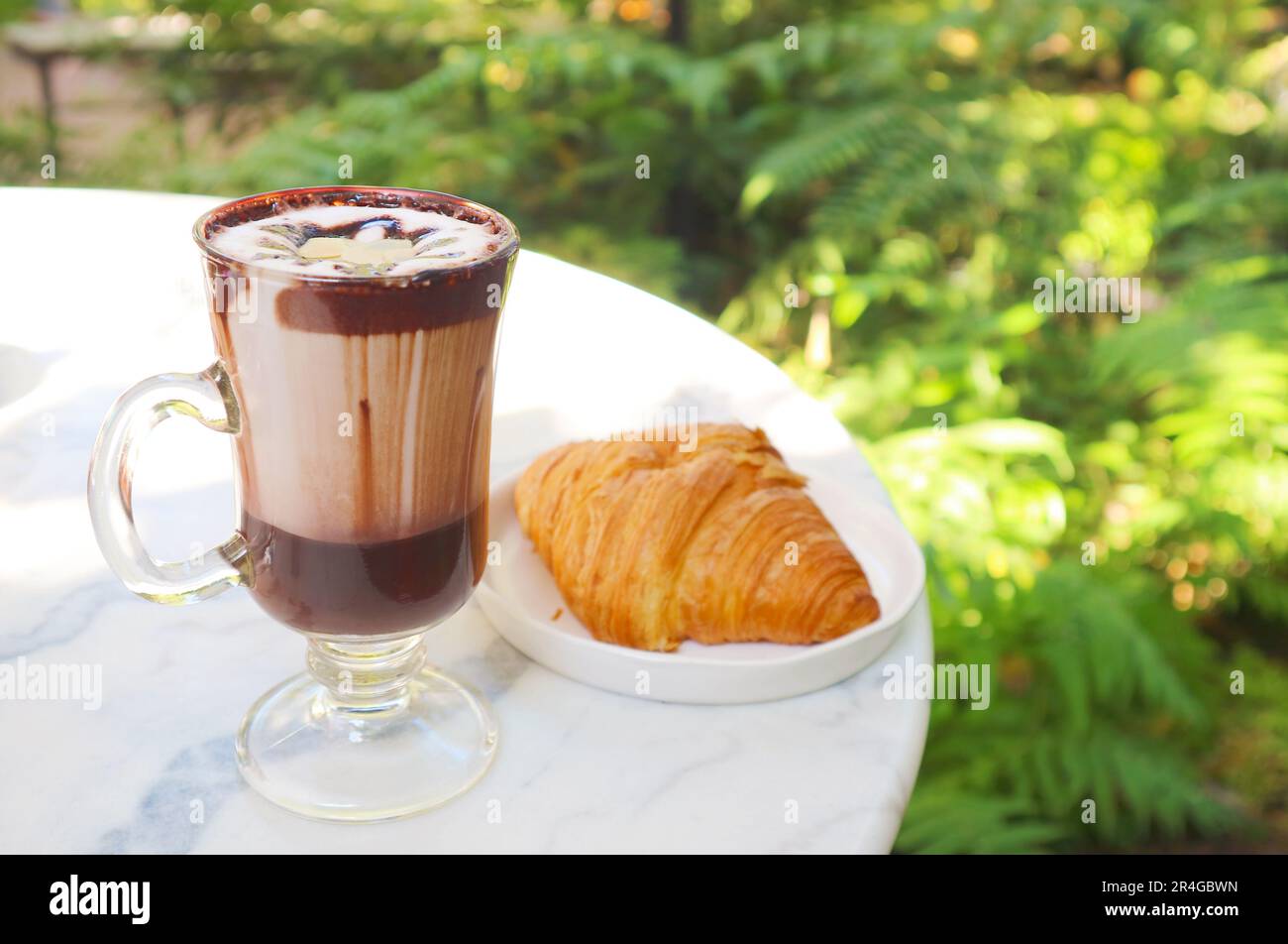 Ein Glas heiße Schokolade mit einem französischen Croissant auf dem weißen Tisch Stockfoto