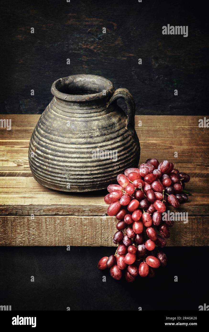 Klassisches Stille Leben mit altem Töpferglas mit roten Trauben auf rustikalem Holzhintergrund Stockfoto