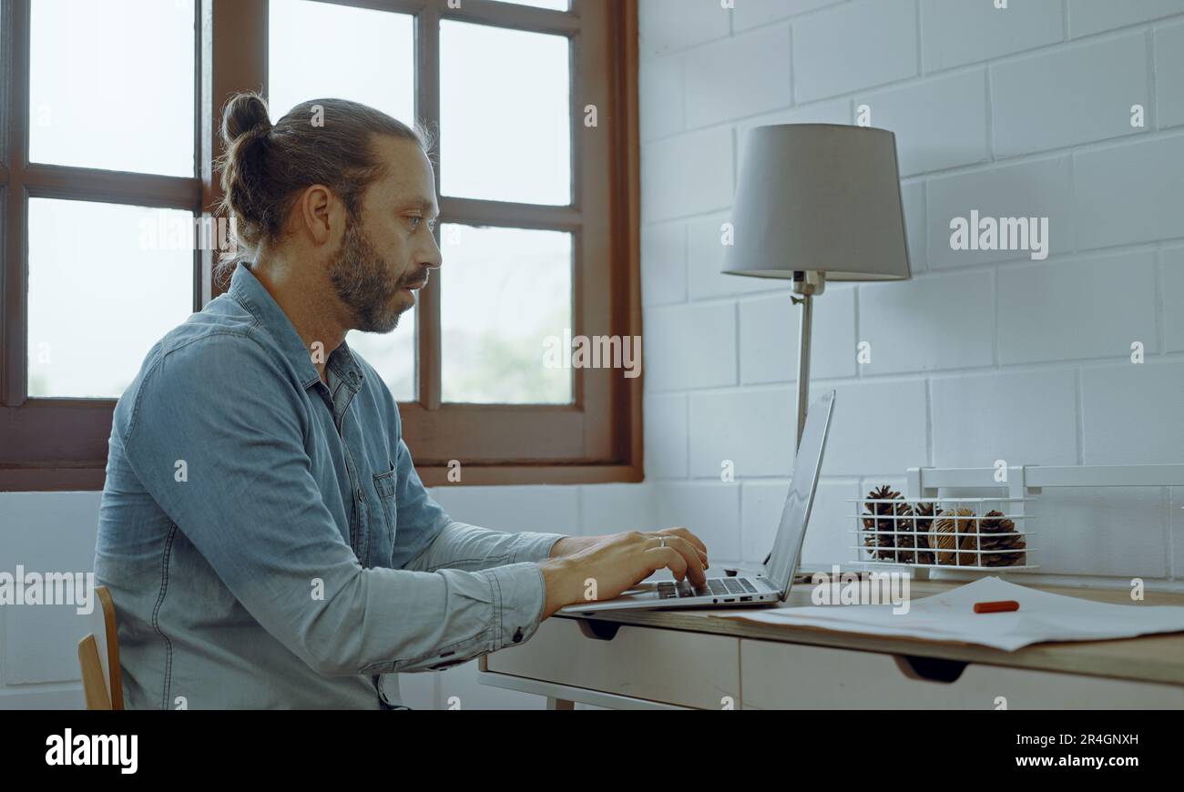 Ein junger besorgter Mann, der auf dem Schreibtisch saß und ein Notebook benutzte. Stockfoto