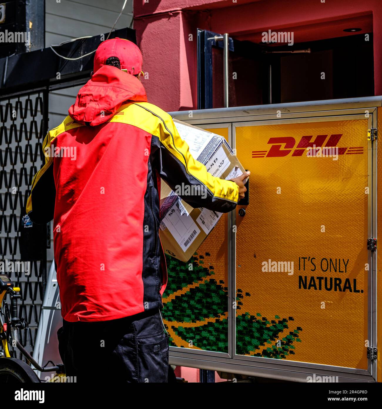 Stavanger, Rogaland, Norwegen, Mai 19 2023, lokaler Arbeiter entlädt und liefert DHL-Pakete oder -Pakete von Einem Markenwagen oder -Wagen Stockfoto